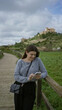© Krakenimages.com - Woman taking selfie on a wooden path with a smartphone in a scenic old town of mallorca, capturing vibrant mediterranean backdrop, smiling in stylish attire.