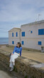 © Krakenimages.com - Woman sitting outdoors by a stone wall in a mediterranean coastal town with blue window shutters and clear skies in mallorca enjoying the scenic seaside view.