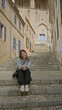 © Krakenimages.com - Woman sitting on stone steps in old mediterranean town of mallorca, wearing casual outfit, smiling, surrounded by historic architecture under sunny weather.