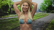 © Krakenimages.com - Woman in blue bikini top holds straw hat above head on street under leafy trees with curved path; happiness.