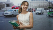 © Krakenimages.com - Young woman holding a stack of books and notebooks, sticks tongue out while smiling on a busy city street; playful student life.