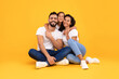 © Prostock-studio - A joyful family sits close together on a vibrant yellow background, smiling warmly as they embrace one another. Their casual outfits add to the cheerful atmosphere of the scene.