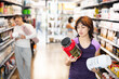 © JackF - Latin girl buyer examines jar of dry food supplement sports nutrition mixture powder, evaluates nutrient content in products. Customers are thinking deciding whether to buy dry protein shake.