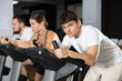 © JackF - In gym, guy does exercises using stationary bicycle. Young group of athletes trains in gym. Physical education and sports, active healthy lifestyle.