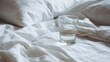 © Jon Stock - Glass of water on a bed with white sheets during morning light in a cozy bedroom setting