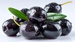 © sungedi - Shiny black pitted fruit cluster rests upon a clean white surface with fresh green leaves