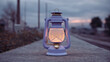 © jianjian - Vintage oil lantern with a warm glowing light standing on a wall during dusk at blue hour with blurred background