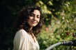 © sogap - A radiant young woman with beautiful dark curly hair smiles serenely embracing the natural beauty of her garden