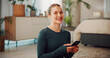 © peopleimages.com - Woman, phone and smile with fitness in home, break and check notification in portrait on floor. Person, smartphone and happy with mobile app, pride or tracking progress for training at house in Spain