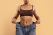 © Anastasiya - Young black woman showing oversized jeans after weightloss. Flat abdomen, defined waist and confident posture highlight transformation, fitness success and body-care motivation themes