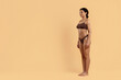 © Anastasiya - Young black woman in brown underwear standing confidently on beige background. Fit natural curves, toned legs and flat abdomen suited for weightloss campaigns, body care and fitness visuals