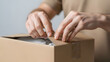 © Violet - Person unpacking a cardboard box with hands and a neutral background