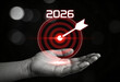 © ATIKUL - Monochrome image hand holding target board with year 2026 and arrow hit center against dark background