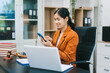 © R Photography - A young Asian woman in a formal blazer works confidently on her laptop in a modern office, surrounded by legal documents and professional tools, reflecting expertise, focus, and a polished corporate