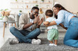 © Prostock-studio - In a warm living room, a baby boy joyfully takes his first steps while his parents cheer him on. The mom helps him from behind, and the dad claps with pride, creating a happy family moment.