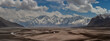 © Travel 'n' Lifestyle - View of stark desert landscape with winding streams contrasts sharply against the majestic snow-capped mountains under a dynamic sky, Skardu, Gilgit Baltistan, Pakistan.