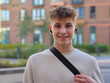 © Pavel Losevsky - Young man wearing a white shirt and black backpack. He is smiling and holding his bag. The background is a brick building