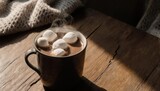 A mug of steaming hot chocolate with marshmallows on a wooden table, beside a knitted blanket