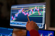 © Studio Marmellata - A person's hand holds a pencil, pointing at a financial chart displayed on a computer monitor, analyzing market trends.