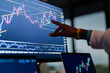 © Studio Marmellata - A person's hand points to a financial chart on a computer screen, analyzing market trends and data.