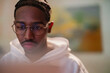 © Studio Marmellata - A young man with braided hair and glasses looks intently at a screen, his face illuminated by its glow.