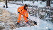 © justsann - Woman in bright orange uniform shoveling snow from a sidewalk in winter.