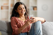 © Home-stock - Happy Indian lady texting on smartphone, browsing social networks or shopping online while relaxing on couch at home in living room