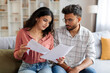 © Home-stock - Focused Indian couple checking bills, reading loan documents, counting monthly spendings, planning family budget while woman holding papers