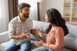 © Home-stock - Angry Indian couple having quarrel experiencing crisis in relationship while sitting on sofa at home. Marital problems, divorce concept