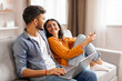 © Home-stock - Happy Hindu couple using laptop and smartphone, looking at each other with smiles and talking while resting on sofa at home