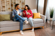 © Home-stock - Happy Indian couple drinking coffee and having conversation, enjoying weekend together at home, sitting on couch in cozy living room, full length