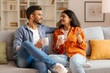 © Home-stock - Domestic pastime. Happy Indian spouses drinking coffee while relaxing on sofa in living room, couple enjoying hot drinks and pleasant conversation