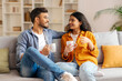 © Home-stock - Coffee and conversations. Indian spouses bonding over hot drink and pleasant talks, sitting on sofa with cups and smiling to each other