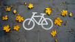 © Mikhail Vorobev - White bicycle lane symbol painted on dark asphalt surrounded by scattered yellow autumn leaves during fall season on a cracked pavement background