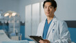 © MALAI Studio - Young asian doctor in lab coat holding a digital tablet inside a modern clinic, professional healthcare worker portrait.