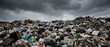 © kiatipol - Massive landfill mountain filled with various types of waste, including plastic bags, furniture, and debris cloudy sky evokes sense