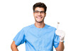 © luismolinero - Young dentist man holding tools over isolated background posing with arms at hip and smiling