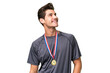 © luismolinero - Young caucasian man with medals over isolated background looking up while smiling