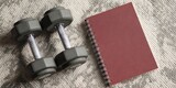 Fitness Journey Companion: A close-up shot of dumbbells and a notebook on a textured surface, evoking themes of exercise, self-improvement, and well-being.
