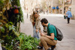 © Drobot Dean - A woman stands hunched over and laughs as she listens to a man sitting next to her near plants while they hold cups
