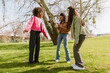© Drobot Dean - A group of three female friends standing on the grass while one of them is talking and one of them is looking at her phone