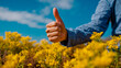 © Nikname - A person's hand giving a thumbs up gesture with a blue and white checkered shirt and yellow flowers in the background