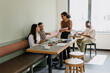 © Drobot Dean - A female worker stands and holds a notebook while smiling and two workers are sitting at a table next to her, one of them talking