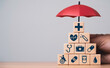© Dilok - Wooden blocks with medical icons in a pyramid under a protective umbrella for health insurance life protection medical coverage wellness support safety and long term healthcare security concept.