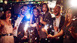 © maxbelchenko - Young friends having fun with sparklers and glasses of champagne at corporate party. Handsome men and woman spend time together, celebrating New Year in cozy space. Сoncept is festive and fun.