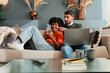 © Jose Calsina - Joyful couple delighting in their shared experience as they use a smartphone and laptop for entertainment and connection at home, fostering a sense of togetherness and enjoyment in their interaction.