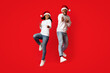 © Prostock-studio - Two friends are dancing and posing playfully in matching red Santa hats and white sweaters. They exude happiness and energy while celebrating the holiday season together.
