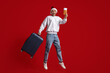 © Prostock-studio - A joyful traveler wearing a Santa hat and casual clothes jumps up, holding a boarding pass and pulling a suitcase. The bright red backdrop adds to the festive atmosphere.