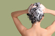 © Pixel-Shot - Young woman applying shampoo on green background, back view