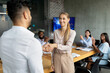 © Prostock-studio - In a modern office setting, a male boss shakes hands with a new female employee while coworkers applaud. The atmosphere is welcoming and positive, encouraging teamwork and collaboration.